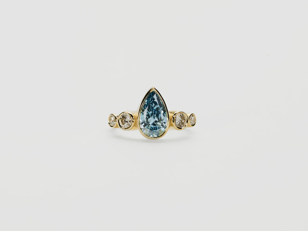 Gold ring with a teardrop-shaped blue diamond  centre stone with round diamonds